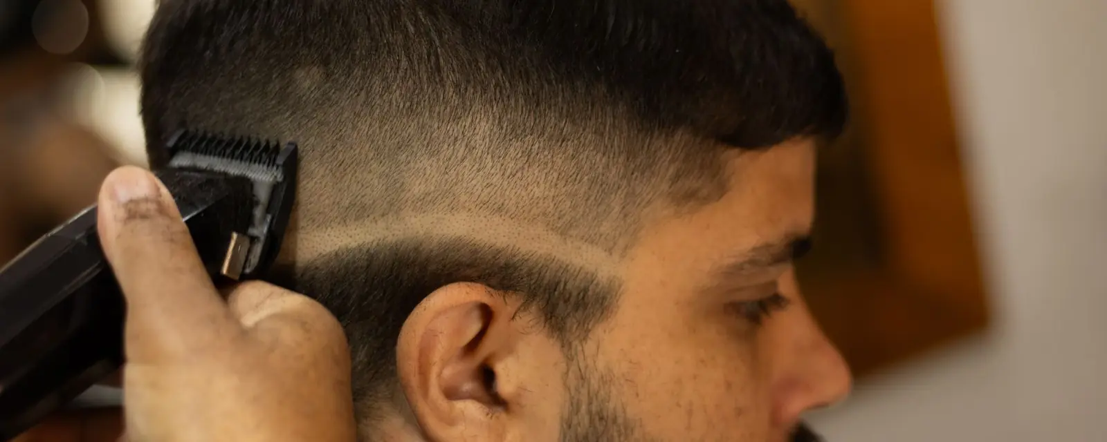 Barbero pasando la máquina por el costado de la cabeza de un cliente de barba corta, marcando la raya del degradé