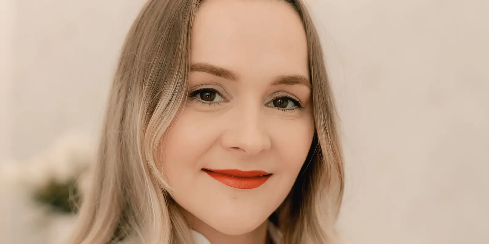 Rostro de frente de una médica rubia de labios rojos que sonríe a cámara en su consultorio de medicina estética